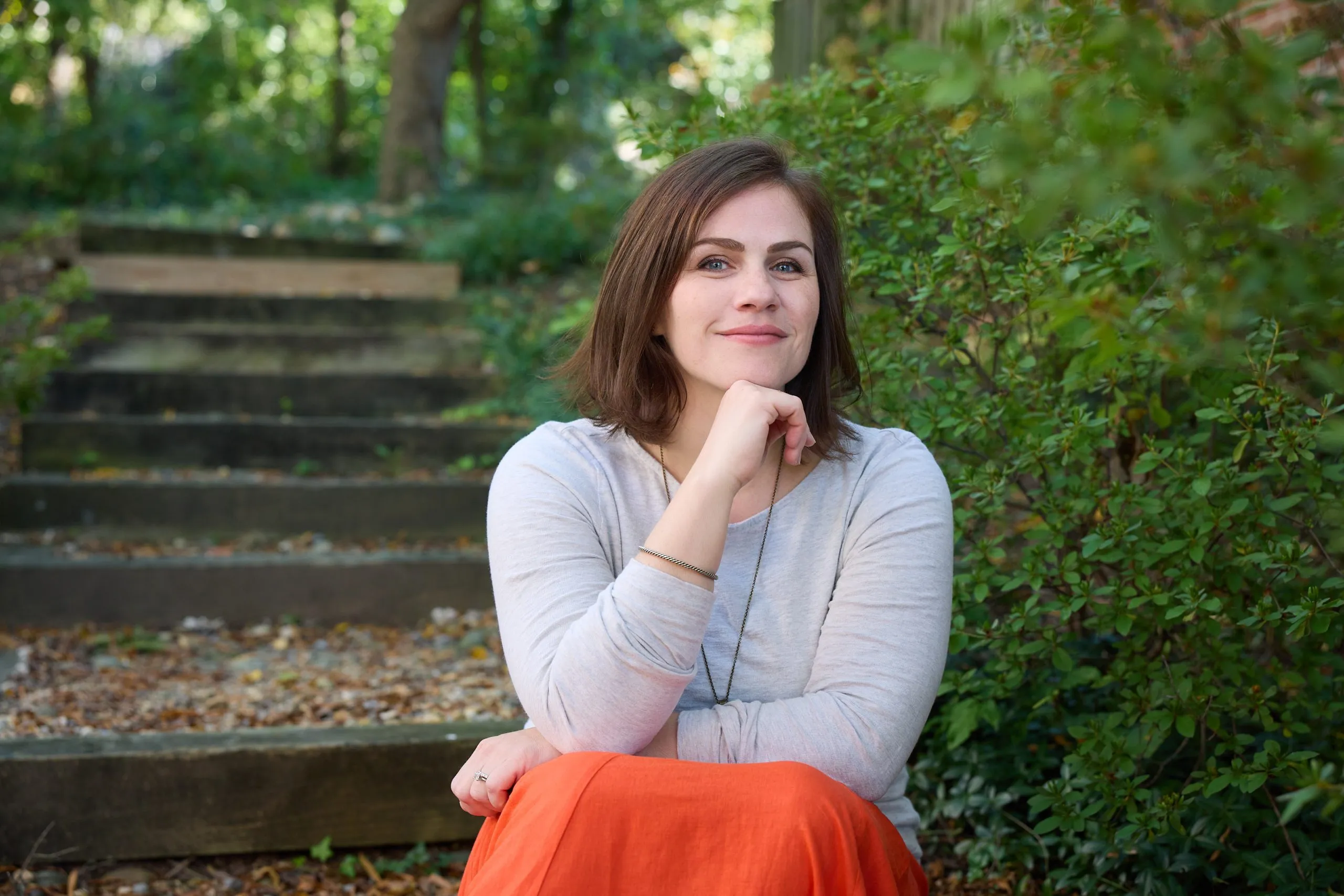 Kristen Kropf seated on a set of garden steps, chin resting on her hand, smiling into the distance.