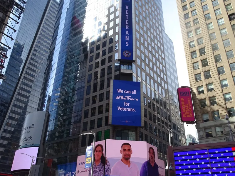 A vertical “Be There for Veterans” banner on a tower in Times Square, New York City.