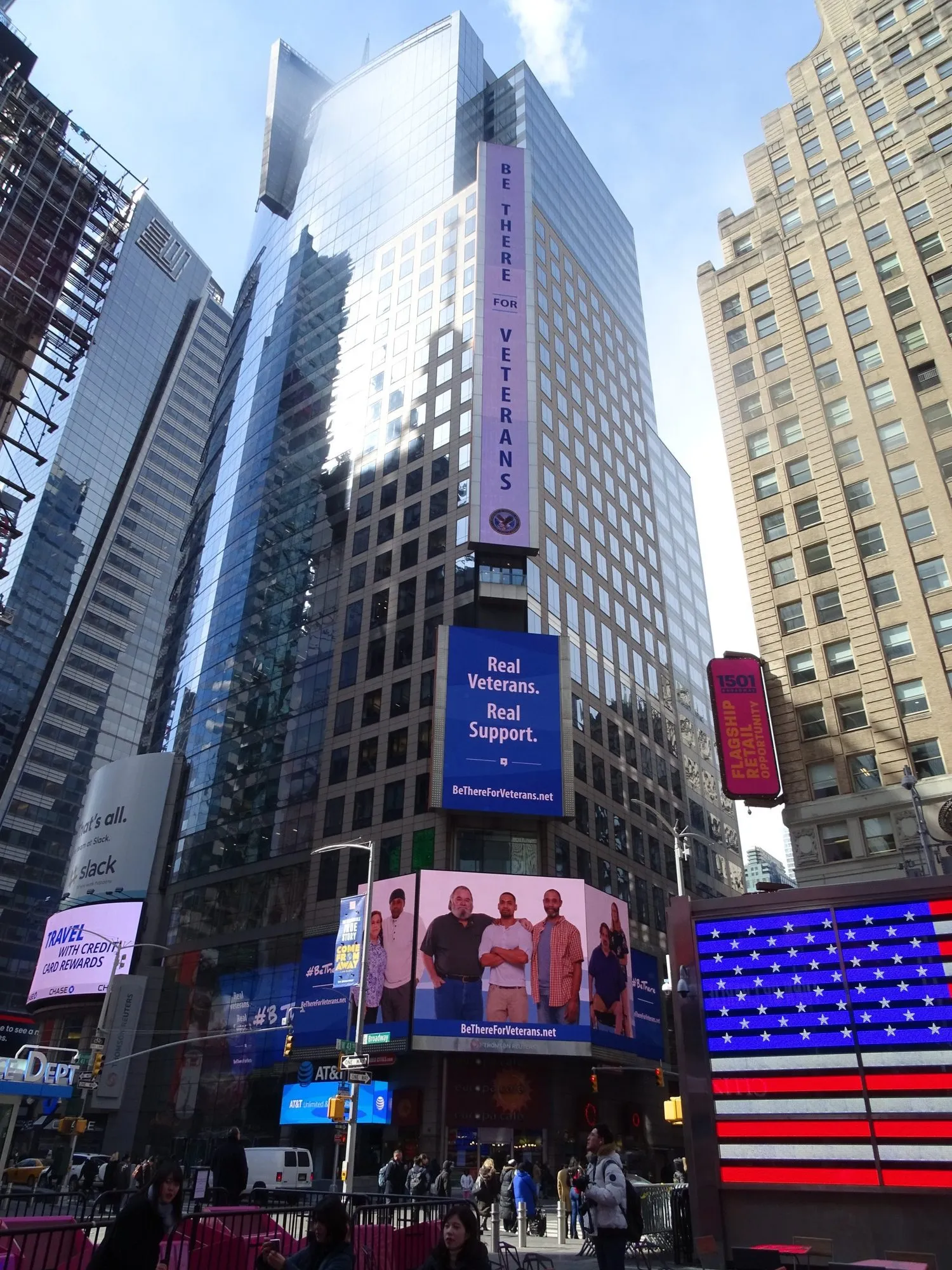 A second Times Square placement of the same banner, lit against the tower at dusk.