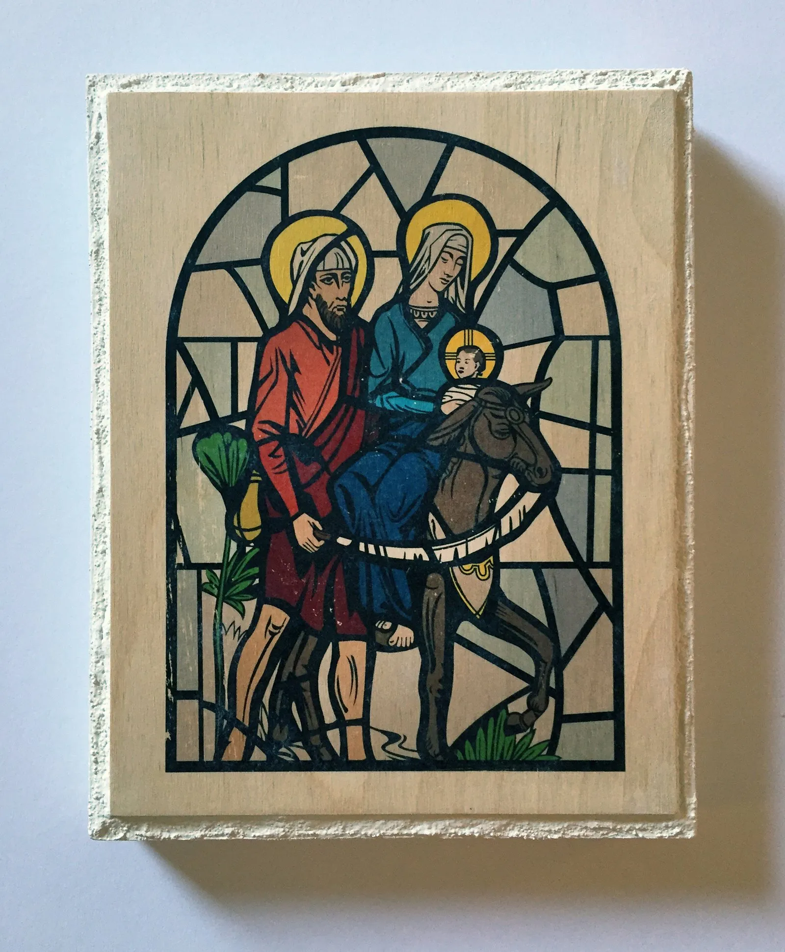 A stained-glass-style Holy Family on the flight into Egypt, transferred onto a raw wood panel.