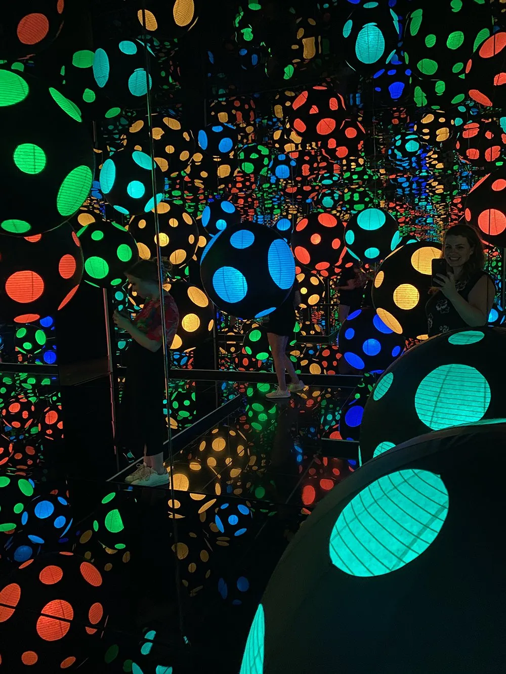 Inside Kusama's Mirror Room — coloured spheres and lanterns reflected endlessly in mirrored walls.