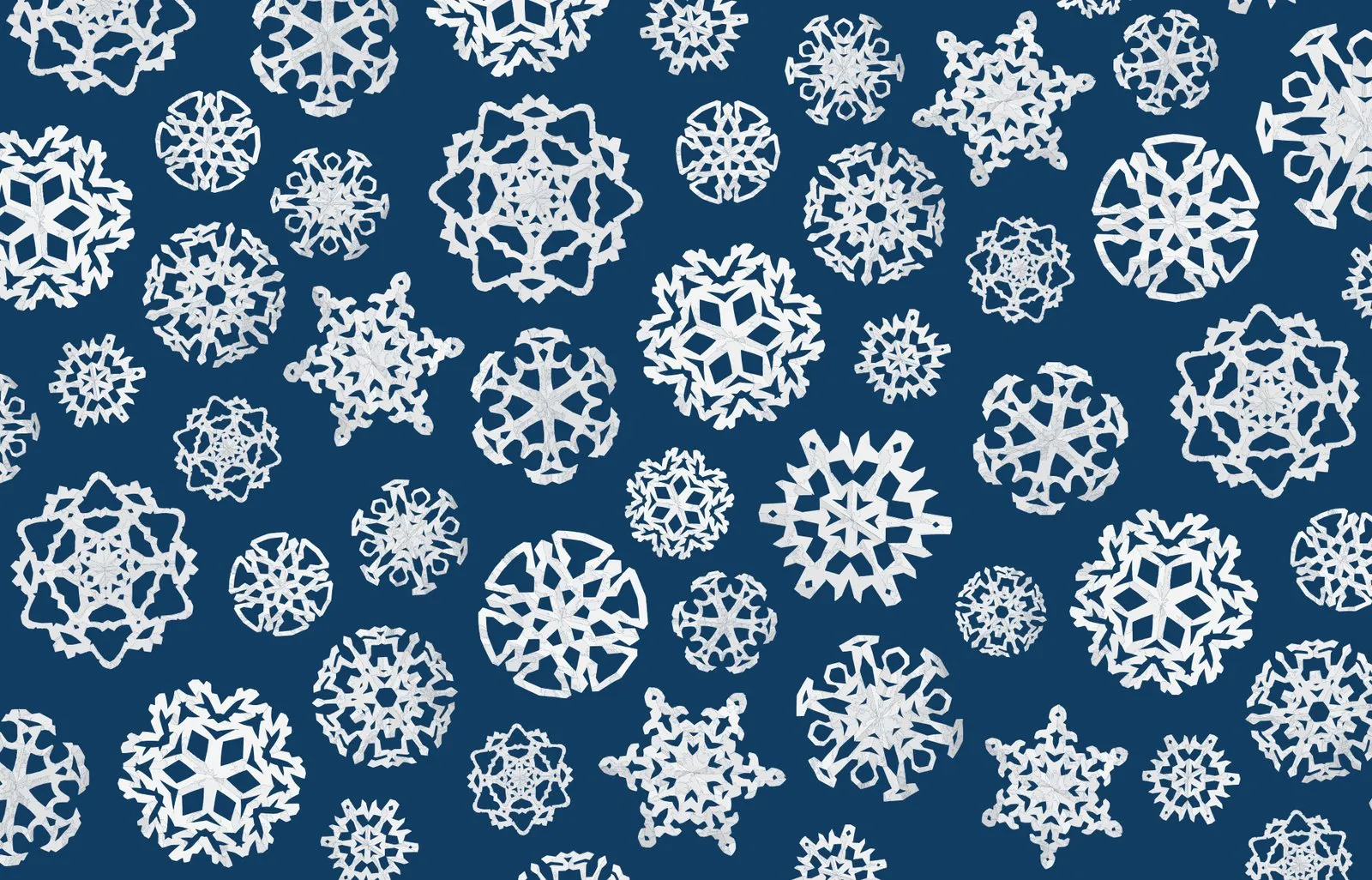 Wrapping paper pattern of white paper-cut snowflakes scattered across navy.