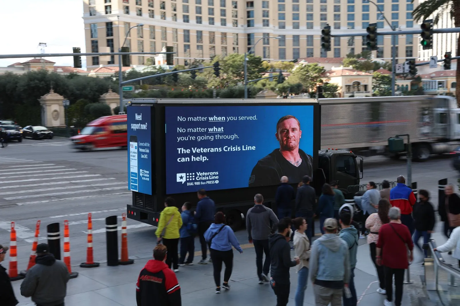 A Veterans Crisis Line digital board on a Las Vegas street during Super Bowl week, crowds passing in front of it.