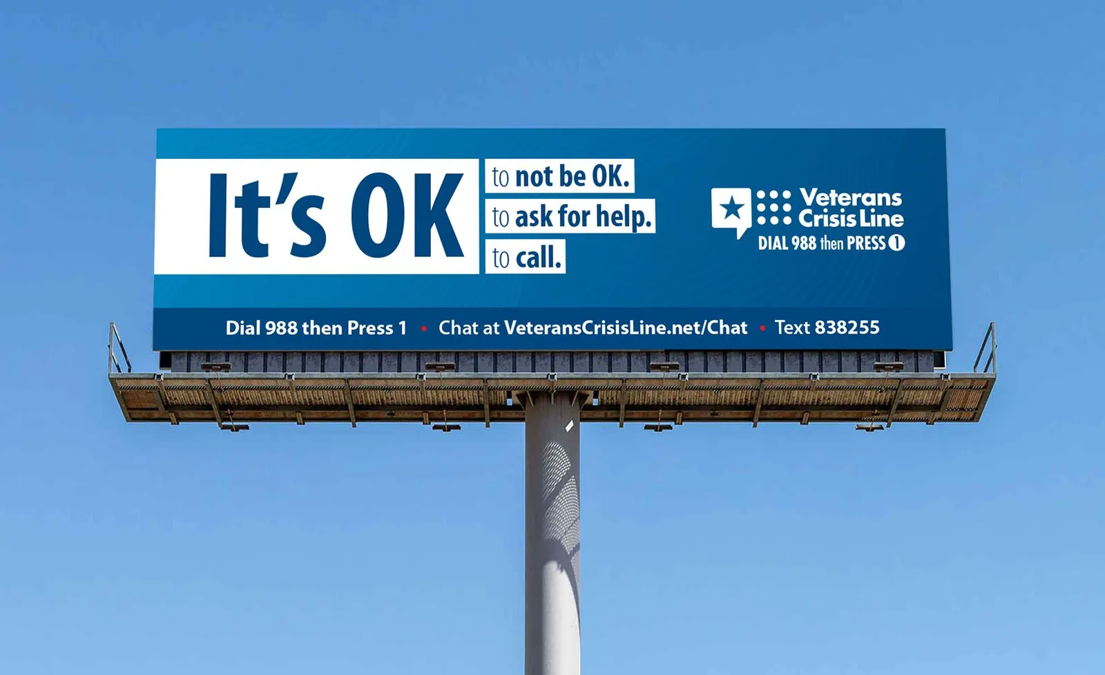 A roadside billboard: “It's OK to not be OK, to ask for help, to call.”, with the hotline and chat details.